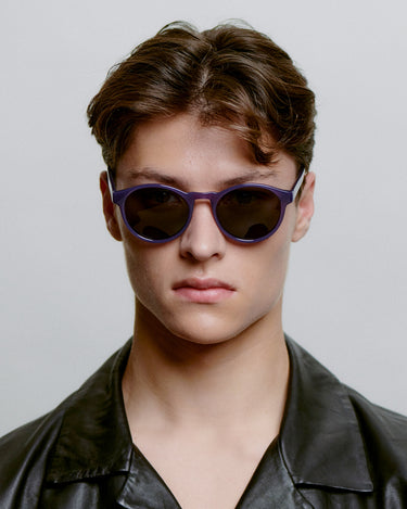 Runde lilla A.Kjærbede solbriller med mørk linse foran på herremodel